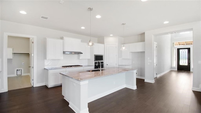 kitchen featuring light stone counters, white cabinetry, an island with sink, and hanging light fixtures