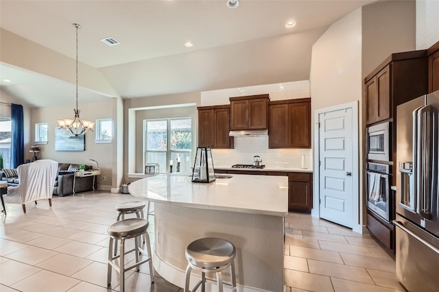 kitchen with a kitchen bar, appliances with stainless steel finishes, a kitchen island with sink, pendant lighting, and an inviting chandelier