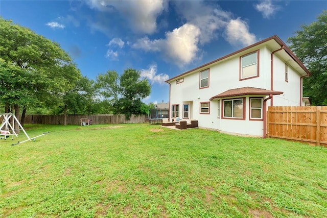 back of property with a trampoline, an outdoor living space, and a yard