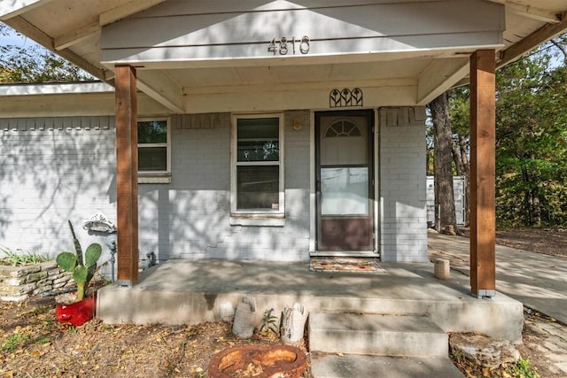 entrance to property featuring a porch and brick siding
