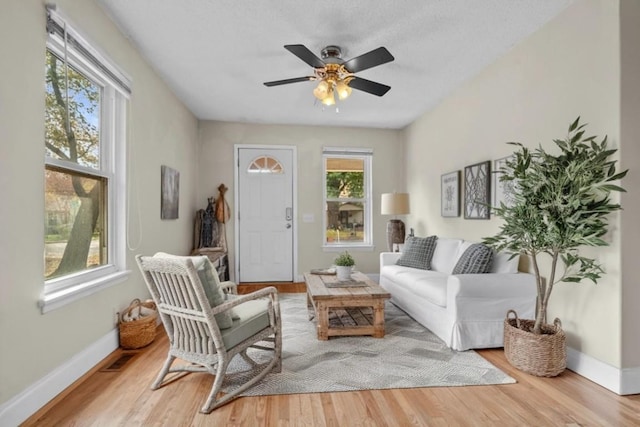 living area featuring wood finished floors, baseboards, and ceiling fan