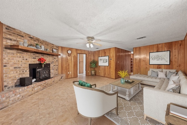 living room featuring ceiling fan, a wood stove, a textured ceiling, and wooden walls