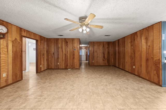 unfurnished room featuring wood walls, ceiling fan, and a textured ceiling