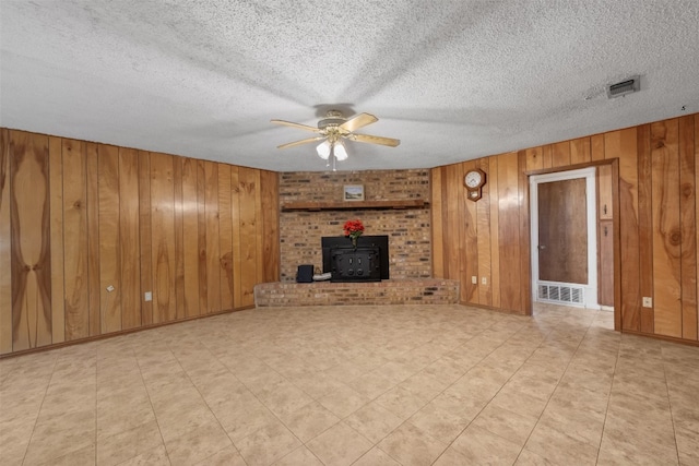 unfurnished living room with a textured ceiling, a wood stove, ceiling fan, and wooden walls