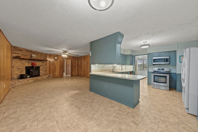 kitchen featuring wood walls, a wood stove, decorative backsplash, kitchen peninsula, and stainless steel appliances