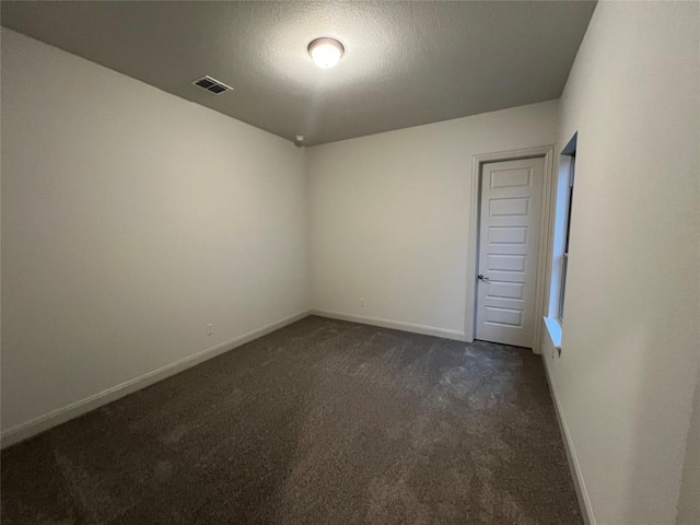 spare room featuring a textured ceiling and dark carpet