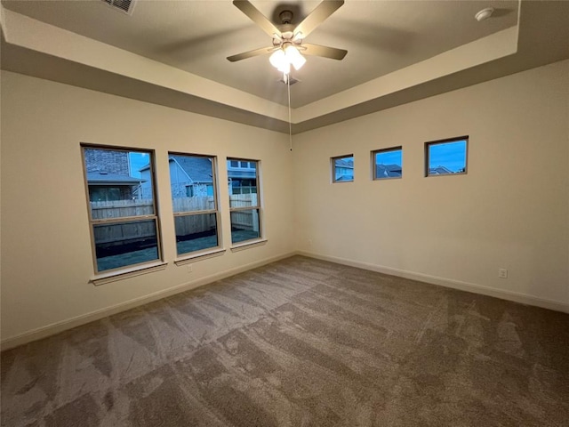 empty room with ceiling fan, a raised ceiling, and carpet