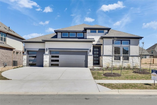 prairie-style house with stucco siding, stone siding, central AC, fence, and concrete driveway