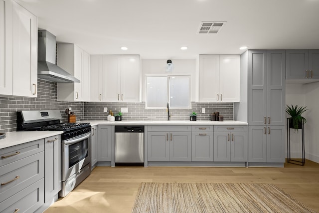 kitchen with gray cabinetry, light hardwood / wood-style floors, wall chimney range hood, and stainless steel appliances