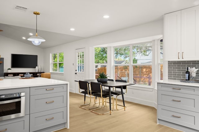 kitchen featuring decorative backsplash, light hardwood / wood-style flooring, pendant lighting, and vaulted ceiling