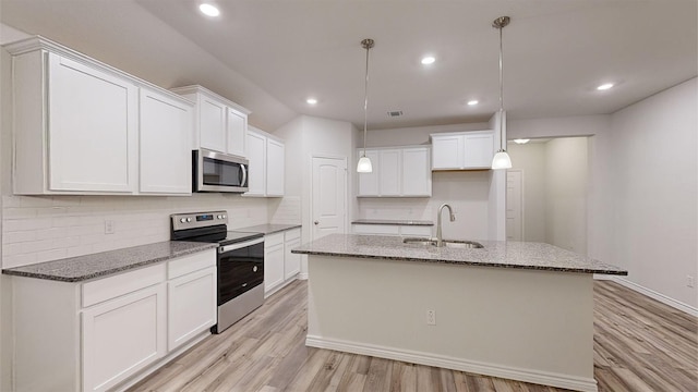 kitchen with dark stone countertops, white cabinetry, a center island with sink, and appliances with stainless steel finishes