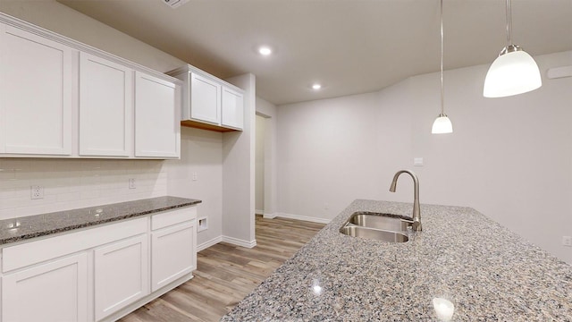 kitchen with dark stone counters, tasteful backsplash, a sink, light wood-style flooring, and white cabinets