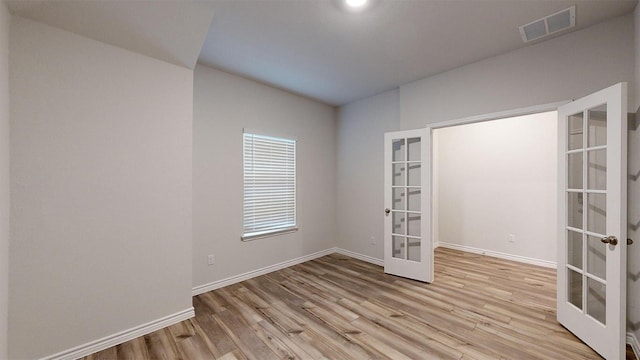 unfurnished room with light wood-type flooring, visible vents, baseboards, and french doors