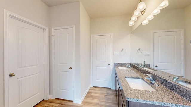 full bath with baseboards, wood finished floors, a sink, and double vanity