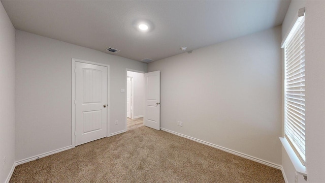 unfurnished bedroom with carpet, visible vents, baseboards, and multiple windows