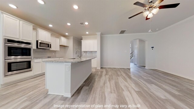 kitchen featuring white cabinetry, an island with sink, stainless steel appliances, and ornamental molding