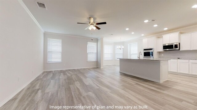 kitchen featuring appliances with stainless steel finishes, ceiling fan with notable chandelier, a kitchen island with sink, crown molding, and white cabinets