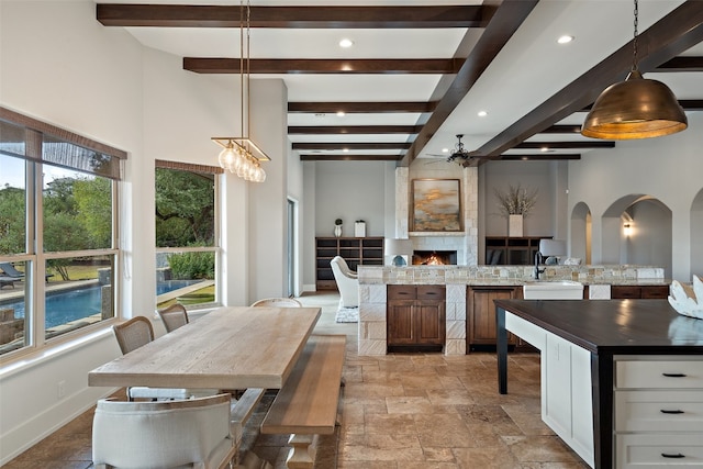 kitchen featuring beamed ceiling, dark stone countertops, pendant lighting, a fireplace, and white cabinets