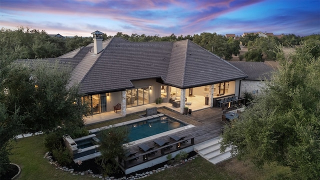 back house at dusk with a swimming pool side deck and a patio area