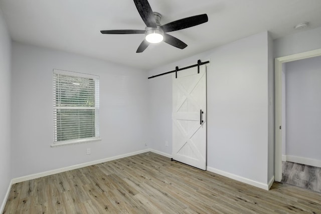 unfurnished bedroom with a barn door, light hardwood / wood-style floors, and ceiling fan