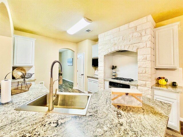 kitchen with stainless steel gas stovetop, hardwood / wood-style floors, white cabinets, and sink