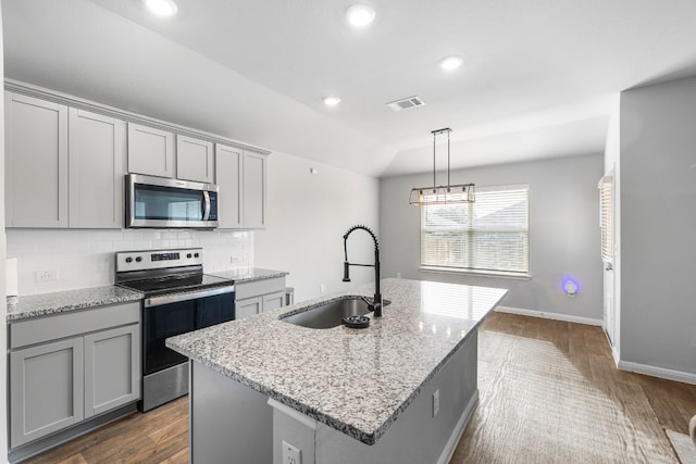 kitchen with a kitchen island with sink, light stone counters, sink, and stainless steel appliances