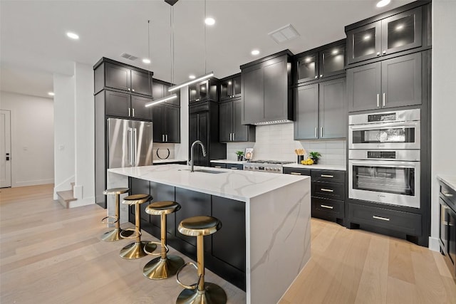 419 Hazeltine Dr, Lakeway, TX 78734 - kitchen with stainless steel appliances, light stone counters, tasteful backsplash, a breakfast bar, and a center island with sink