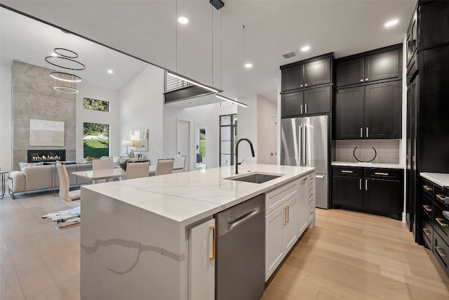 kitchen with sink, light stone countertops, an island with sink, appliances with stainless steel finishes, and a tiled fireplace