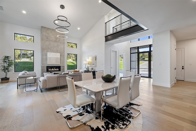 dining room with light wood-type flooring, a fireplace, high vaulted ceiling, and a chandelier