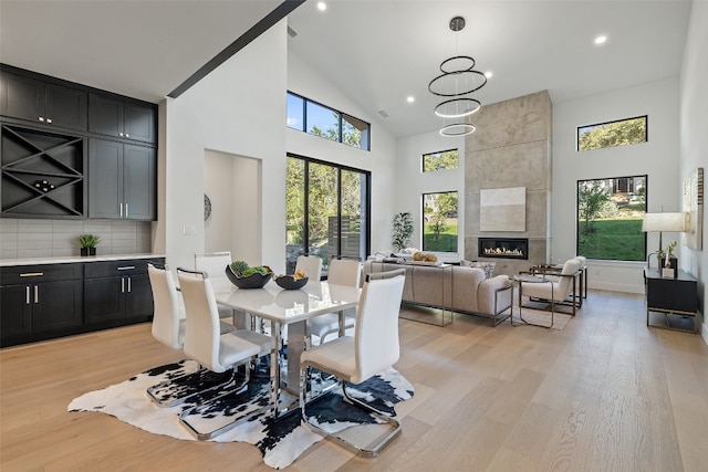 dining area with a tile fireplace, high vaulted ceiling, a chandelier, and light wood-type flooring