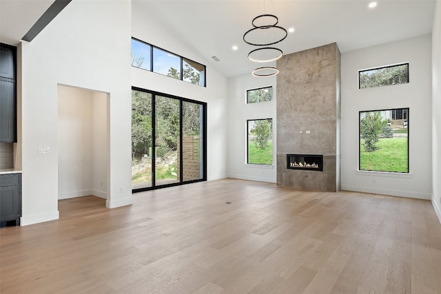 unfurnished living room with high vaulted ceiling, light hardwood / wood-style floors, a tile fireplace, and a wealth of natural light