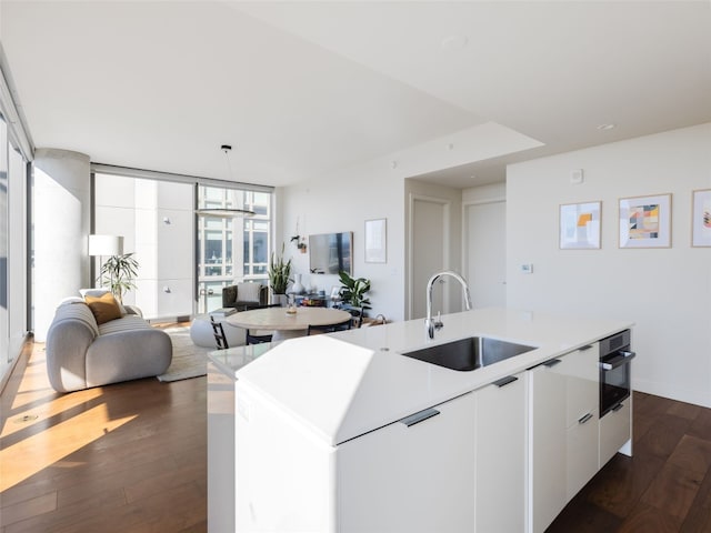 kitchen featuring dark hardwood / wood-style flooring, sink, a center island with sink, white cabinets, and oven