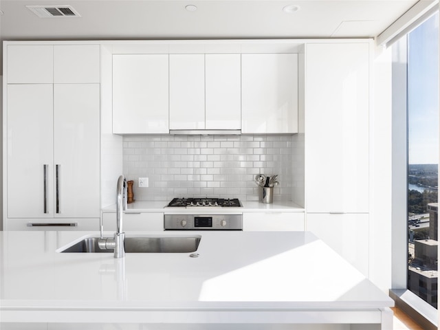 kitchen featuring backsplash, sink, white cabinets, and stainless steel gas cooktop