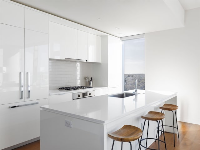 kitchen featuring sink, light hardwood / wood-style flooring, backsplash, an island with sink, and white cabinets