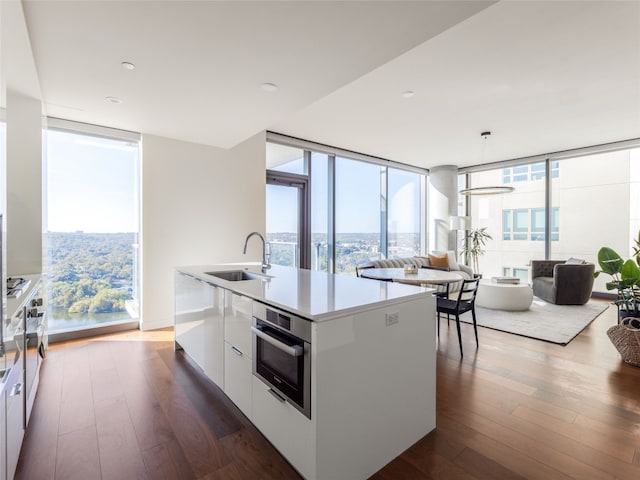 kitchen with dark hardwood / wood-style flooring, sink, white cabinets, oven, and an island with sink