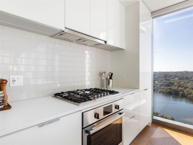 kitchen with appliances with stainless steel finishes, tasteful backsplash, light hardwood / wood-style flooring, white cabinetry, and range hood