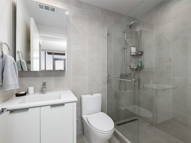 bathroom with vanity, toilet, a tile shower, and tile walls