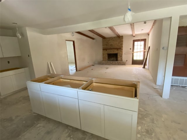 kitchen with a fireplace, beam ceiling, and white cabinetry