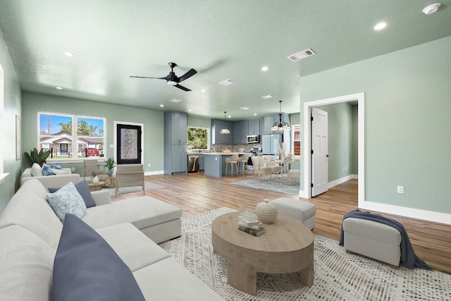 living room featuring light wood-type flooring, a textured ceiling, and ceiling fan with notable chandelier