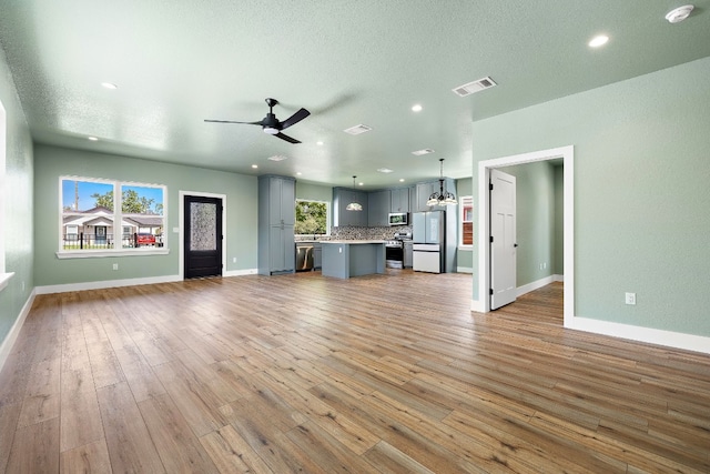 unfurnished living room with ceiling fan with notable chandelier, light wood-type flooring, and a textured ceiling