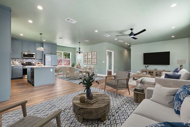 living room featuring ceiling fan with notable chandelier and light wood-type flooring