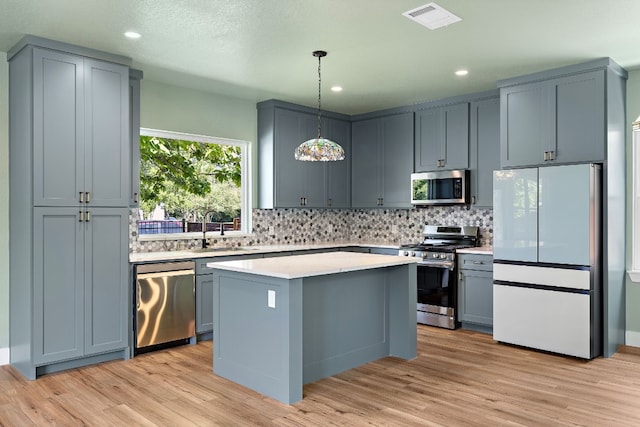 kitchen featuring appliances with stainless steel finishes, sink, pendant lighting, a center island, and light hardwood / wood-style floors