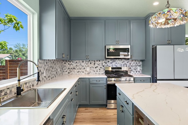 kitchen featuring sink, light stone counters, pendant lighting, decorative backsplash, and appliances with stainless steel finishes