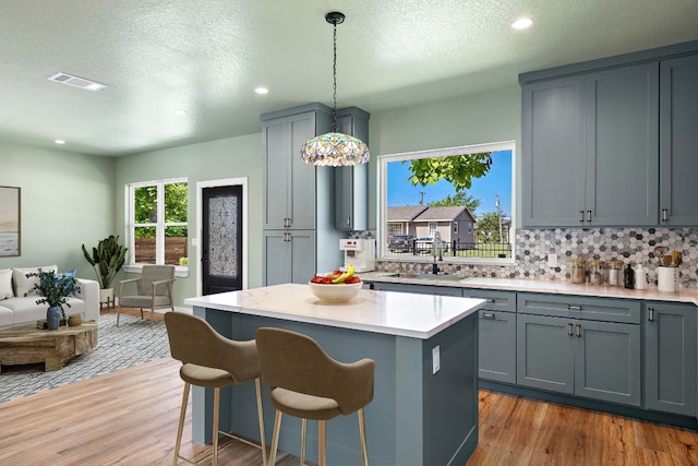 kitchen with gray cabinetry, a center island, backsplash, sink, and hanging light fixtures