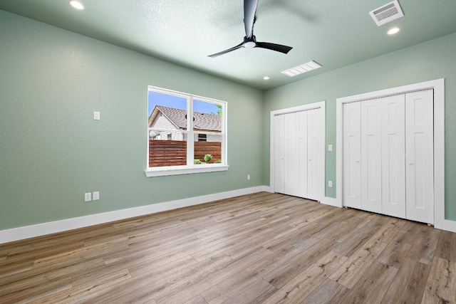 unfurnished bedroom with ceiling fan, light wood-type flooring, a textured ceiling, and two closets