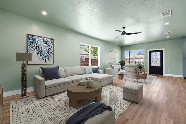 living room featuring ceiling fan, light hardwood / wood-style floors, and a textured ceiling