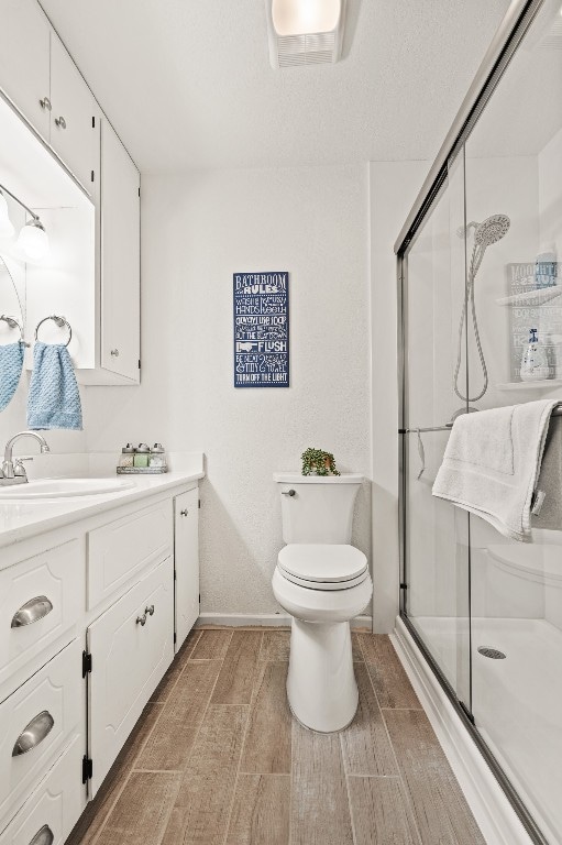 bathroom with hardwood / wood-style flooring, vanity, toilet, and an enclosed shower