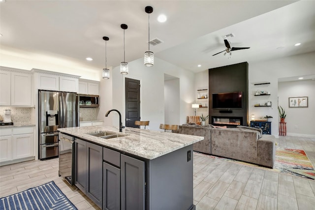 kitchen with a kitchen island with sink, sink, ceiling fan, light stone counters, and white cabinetry