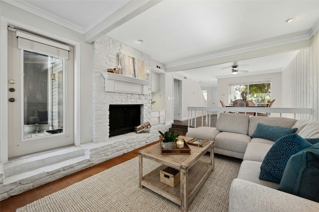 living room with ceiling fan, a fireplace, hardwood / wood-style floors, beam ceiling, and crown molding