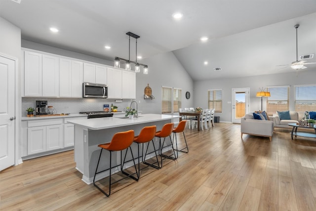 kitchen with light hardwood / wood-style floors, white cabinetry, stainless steel appliances, and an island with sink